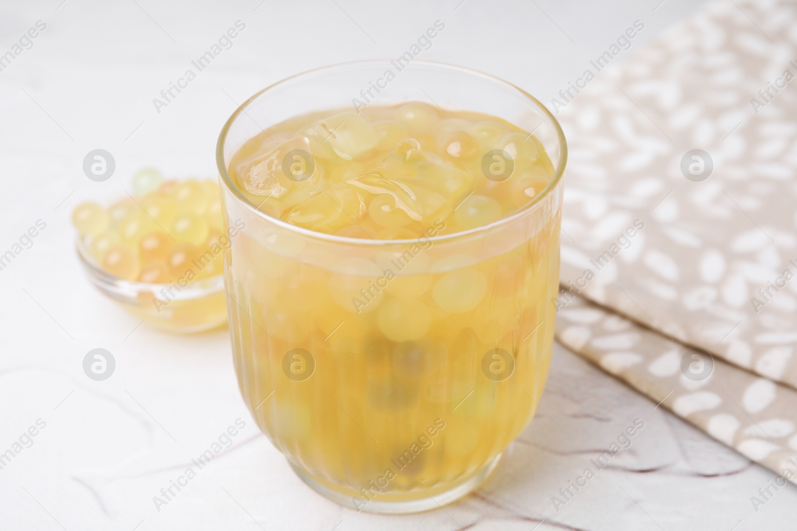 Photo of Tasty bubble tea in glass and tapioca pearls on white table, closeup