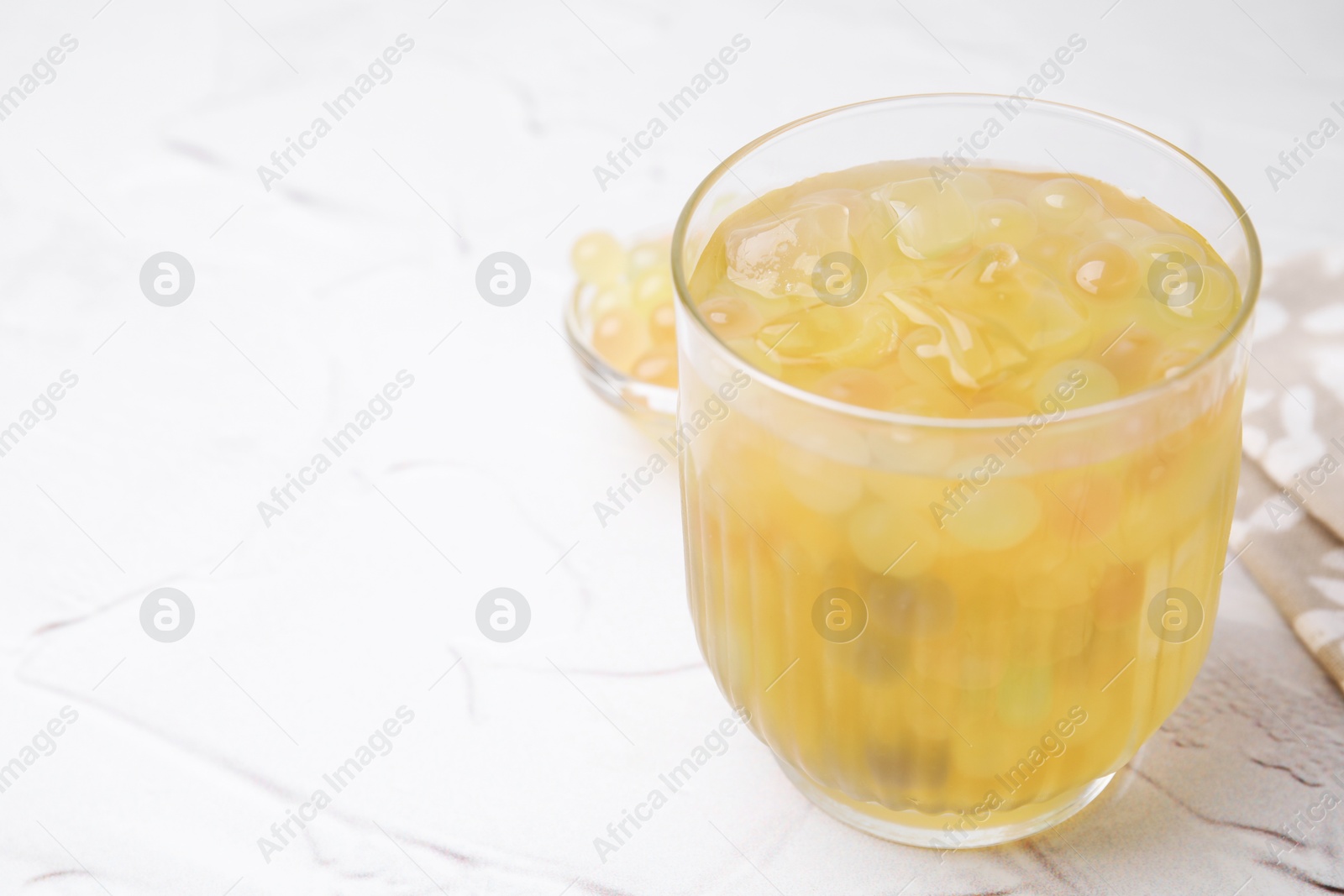 Photo of Tasty bubble tea in glass and tapioca pearls on white table, closeup. Space for text