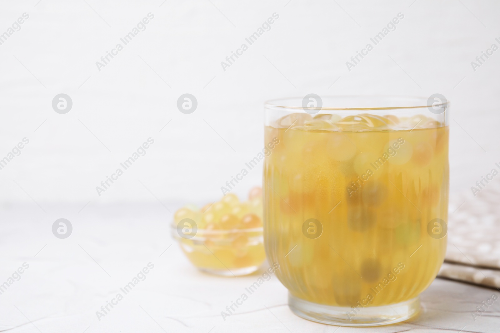 Photo of Tasty bubble tea in glass and tapioca pearls on white table, closeup. Space for text