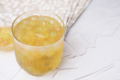 Photo of Tasty bubble tea in glass and tapioca pearls on white table, closeup. Space for text