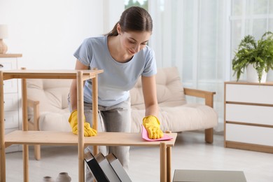 Young woman cleaning wooden shelf with rag at home