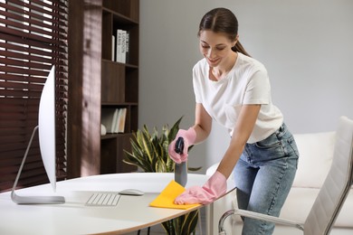 Young woman cleaning table with rag and spray in office