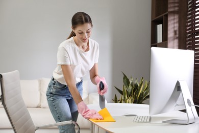 Young woman cleaning table with rag and spray in office