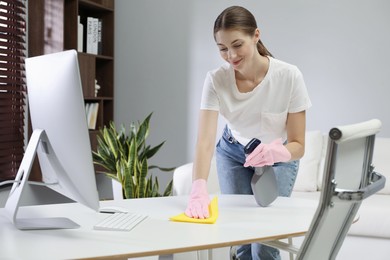 Photo of Young woman cleaning table with rag and spray in office