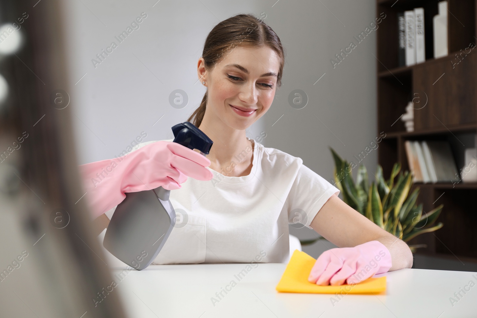 Photo of Young woman cleaning table with rag and spray in office