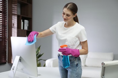 Photo of Young woman cleaning computer with rag and spray in office