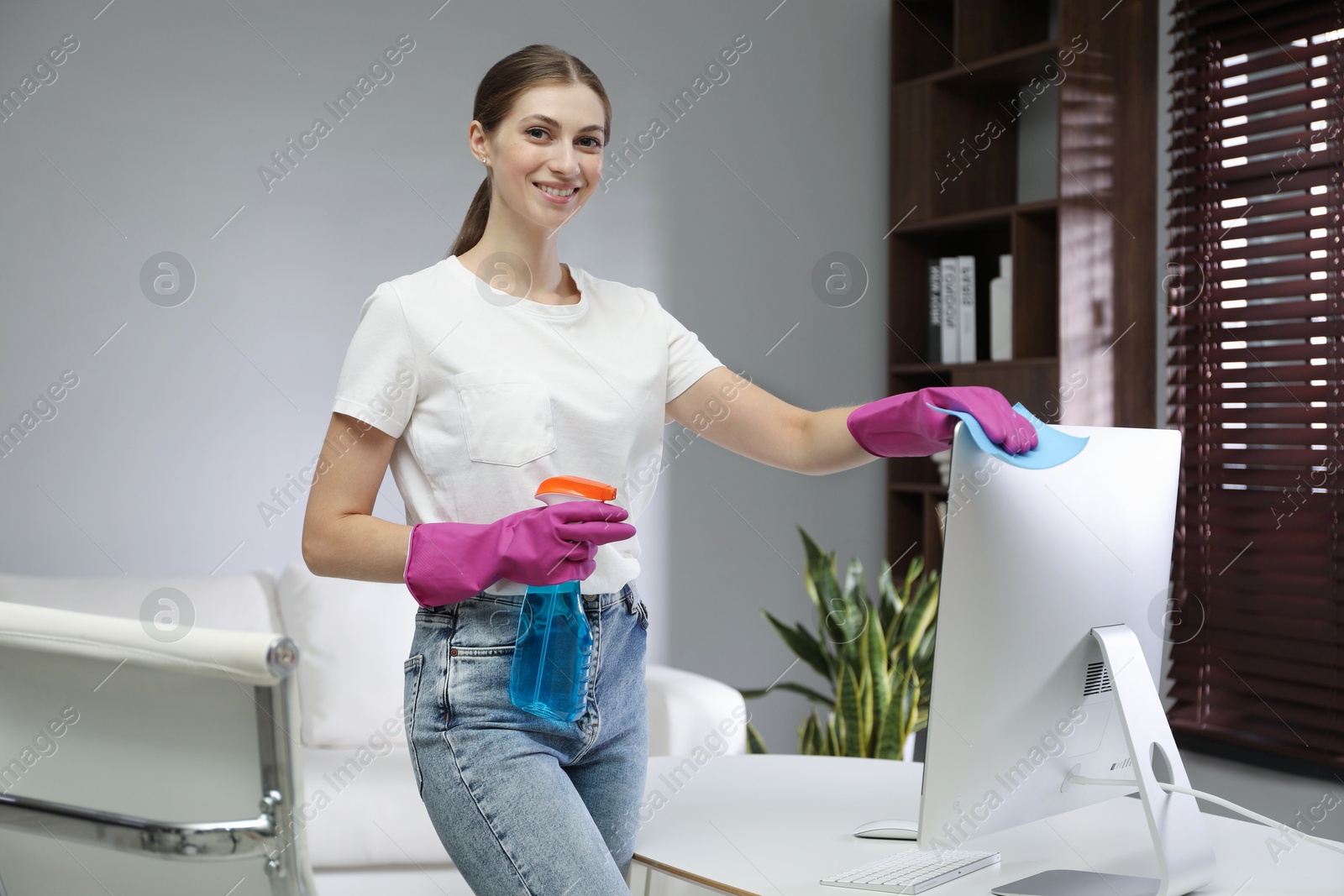 Photo of Young woman cleaning computer with rag and spray in office