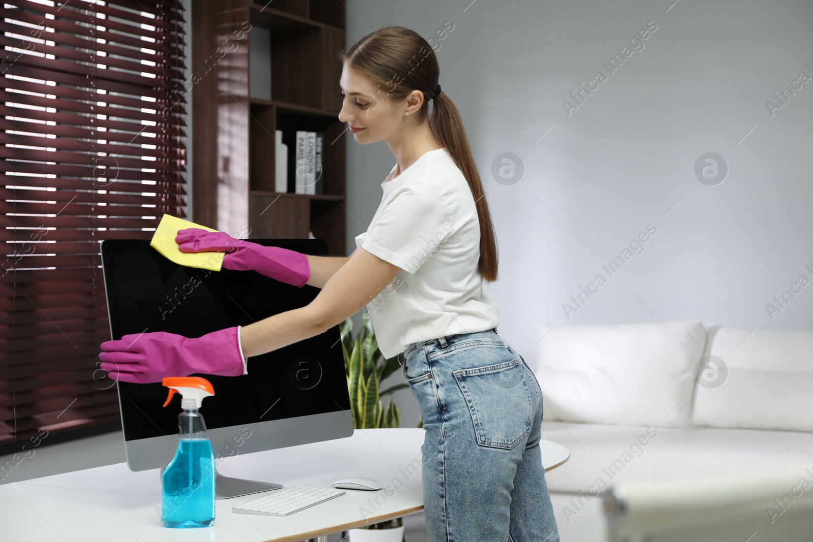 Photo of Young woman cleaning computer with rag and spray in office