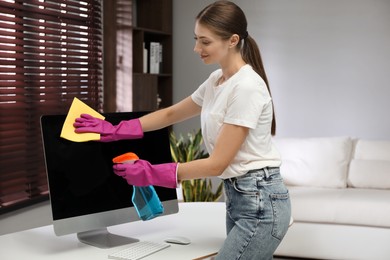 Photo of Young woman cleaning computer with rag and spray in office