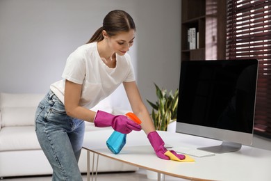 Photo of Young woman cleaning table with rag and spray in office