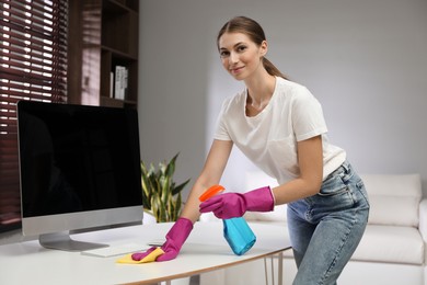 Photo of Young woman cleaning table with rag and spray in office