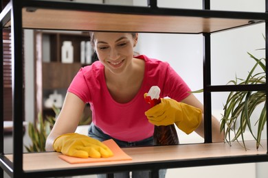 Young woman cleaning wooden shelf with rag and spray in office