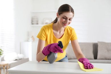 Photo of Young woman cleaning table with rag and spray in office