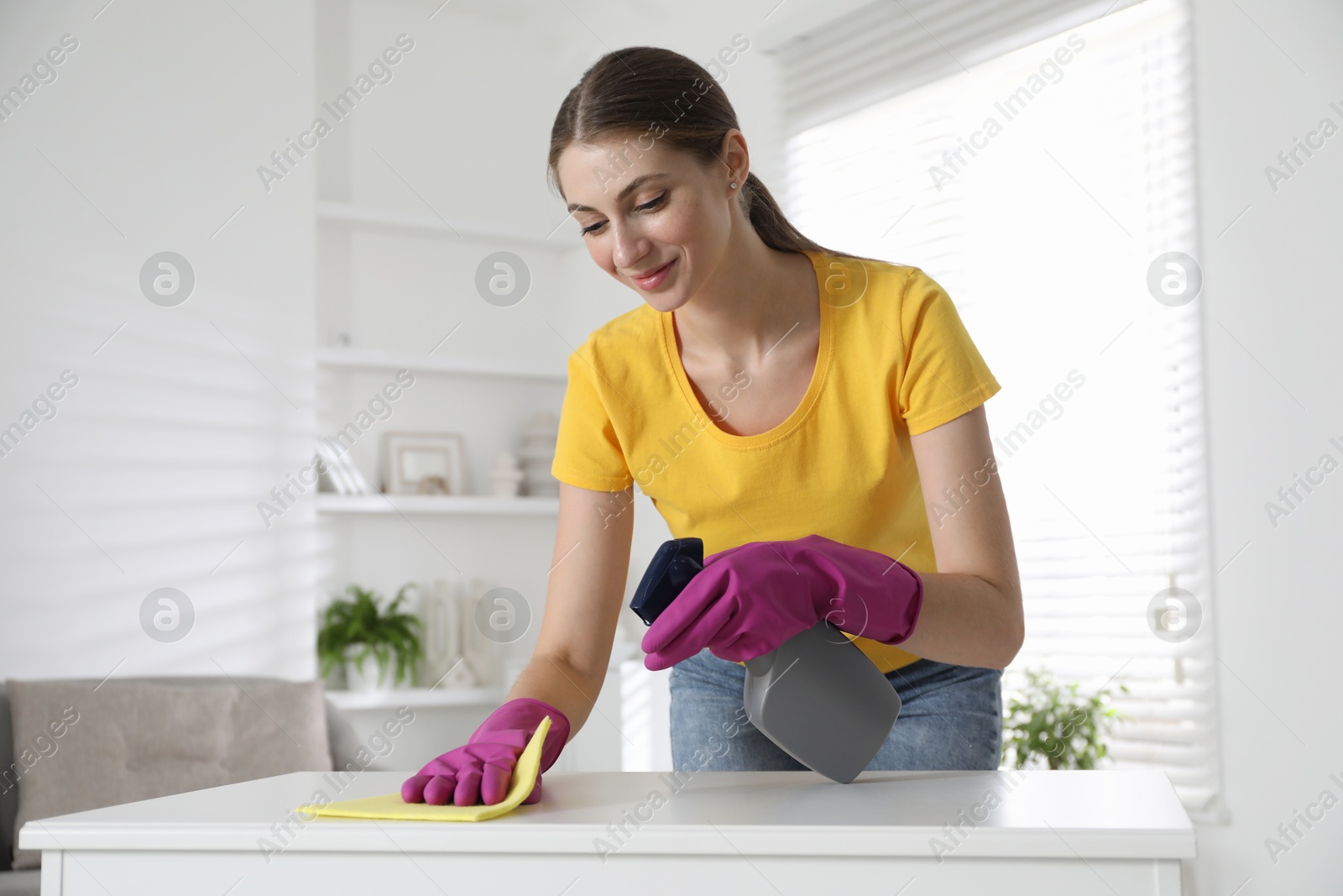 Photo of Young woman cleaning table with rag and spray in office