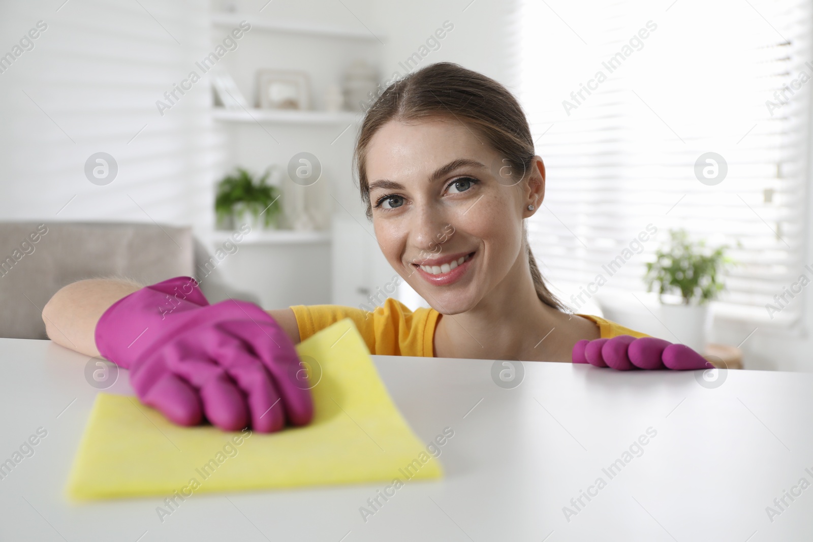 Photo of Young woman cleaning table with rag in office