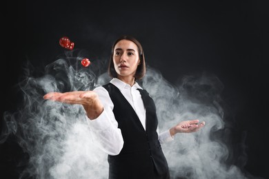 Photo of Croupier holding casino chips and dice on black background with smoke