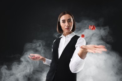 Photo of Croupier holding casino chips and dice on black background with smoke