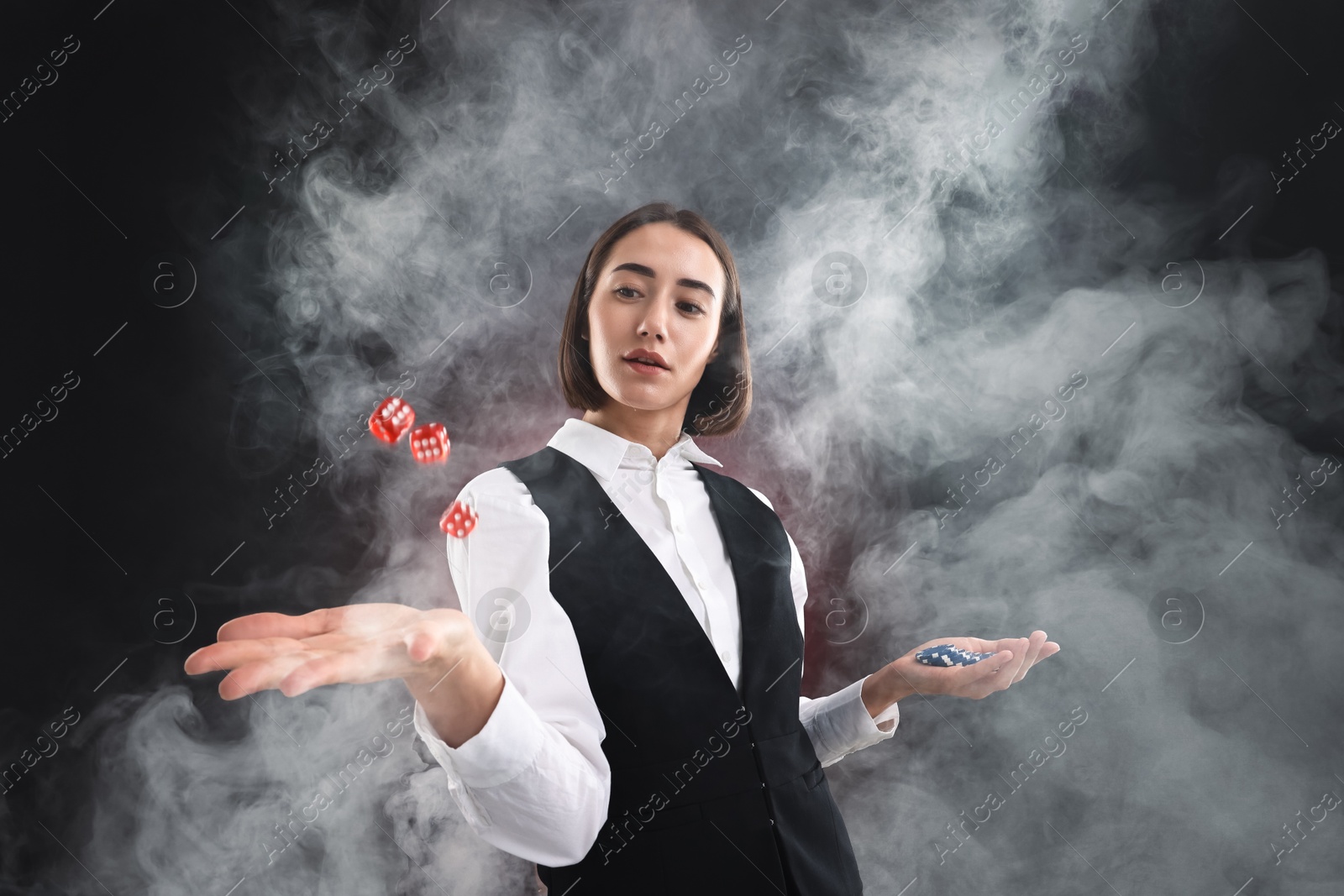 Photo of Croupier holding casino chips and dice on dark red background with smoke