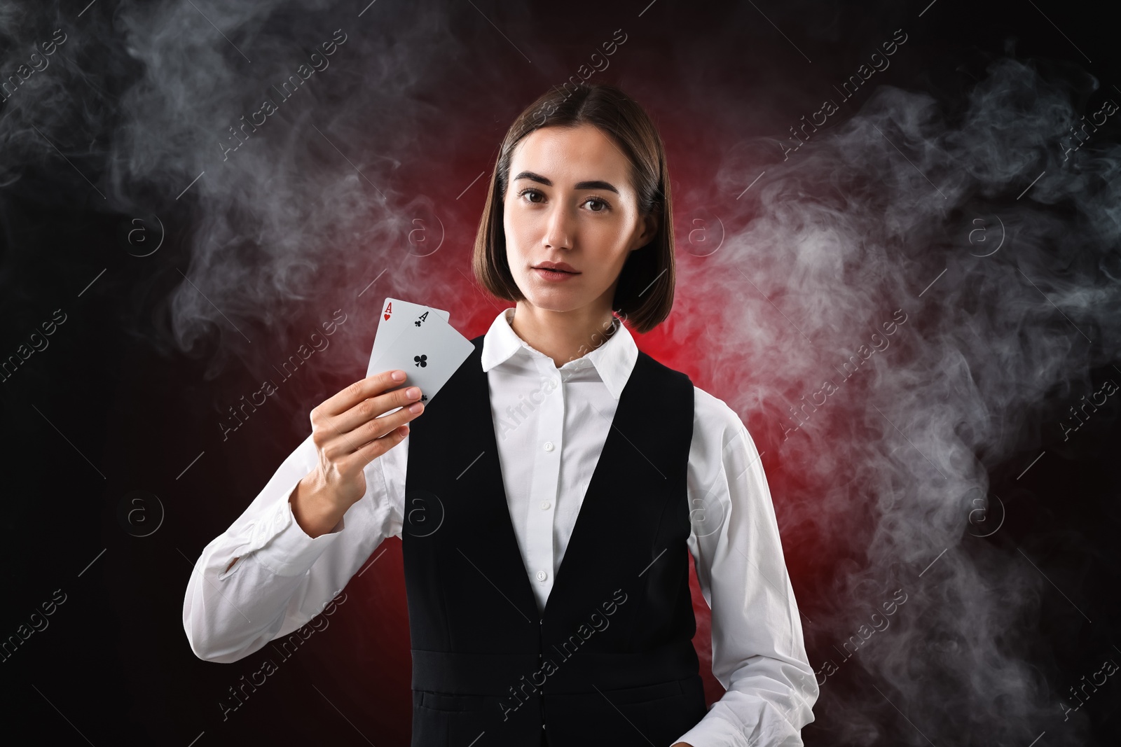 Photo of Croupier holding playing cards on dark red background with smoke