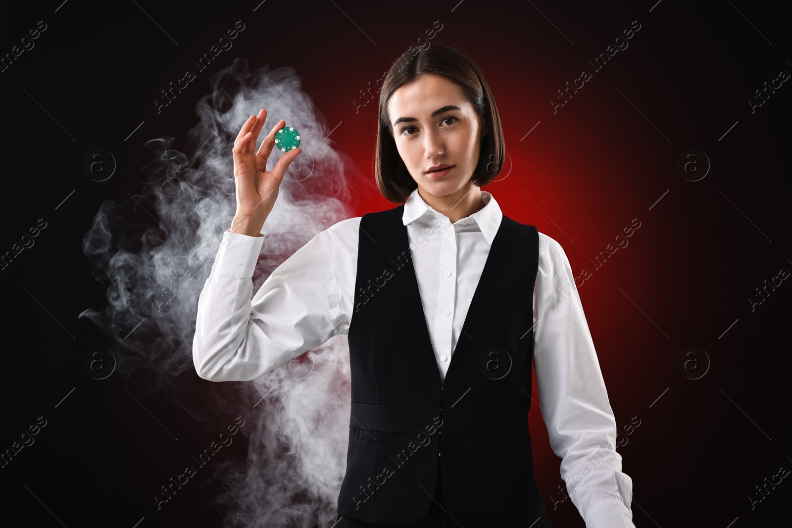 Photo of Croupier holding casino chip on dark red background with smoke