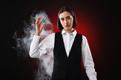 Photo of Croupier holding casino chip on dark red background with smoke