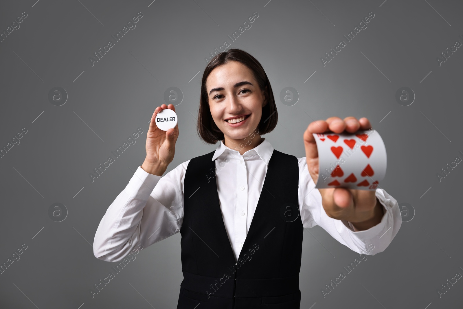 Photo of Professional croupier with cards and dealer button on grey background