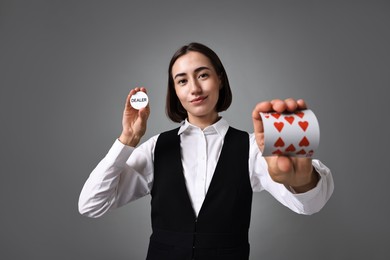 Professional croupier with cards and dealer button on grey background