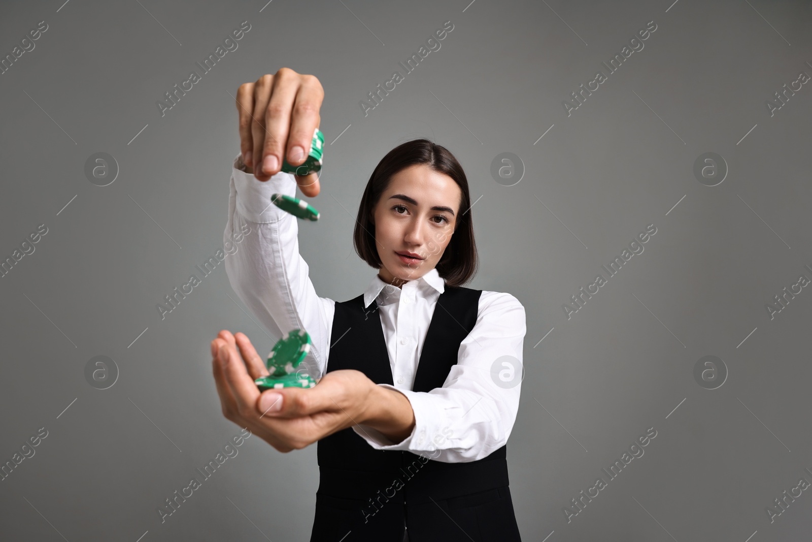 Photo of Professional croupier with casino chips on grey background