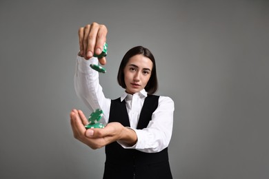 Professional croupier with casino chips on grey background