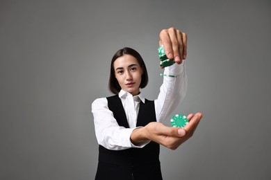 Professional croupier with casino chips on grey background