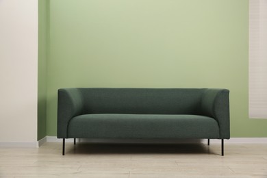 Photo of One stylish sofa near green wall indoors