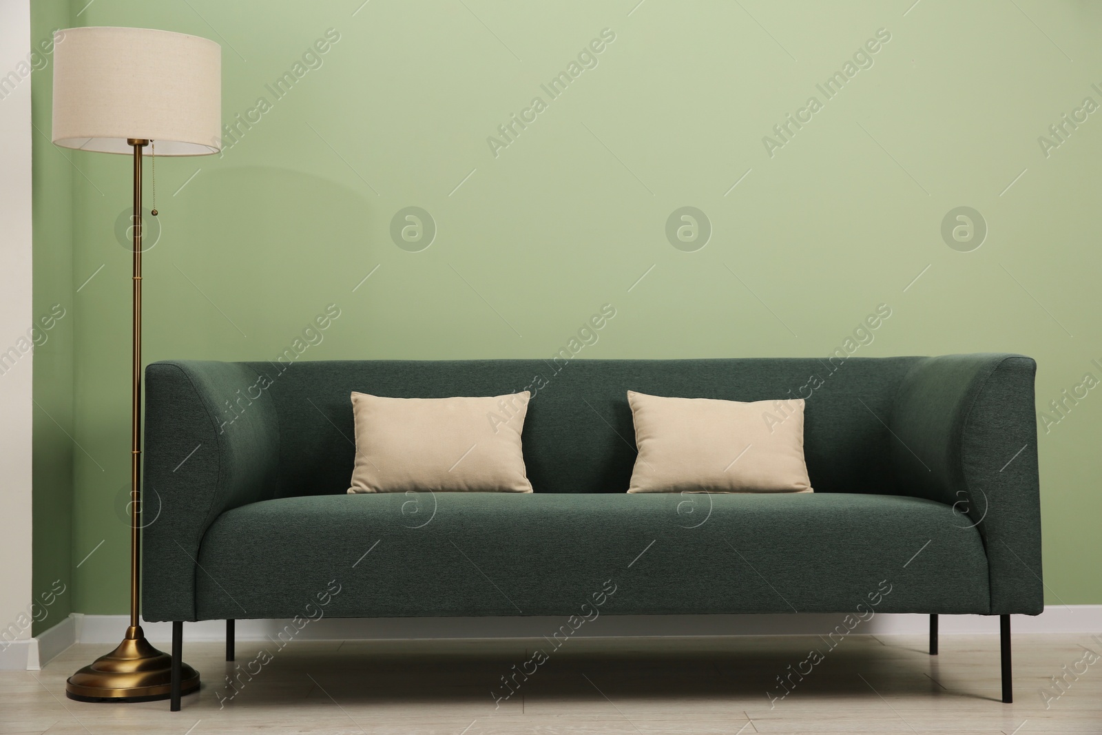 Photo of Stylish sofa with pillows and lamp near green wall indoors