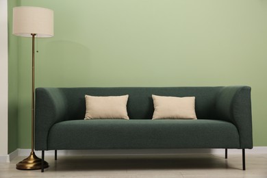 Stylish sofa with pillows and lamp near green wall indoors