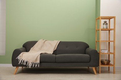 Stylish sofa with blanket and shelving unit near green wall indoors