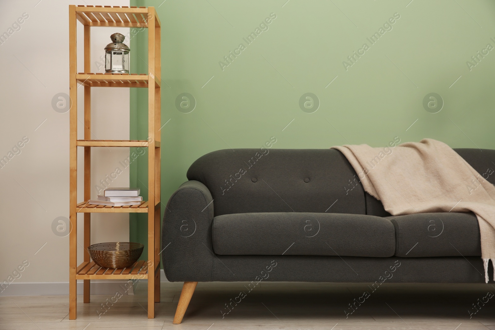 Photo of Stylish sofa with blanket and shelving unit near green wall indoors