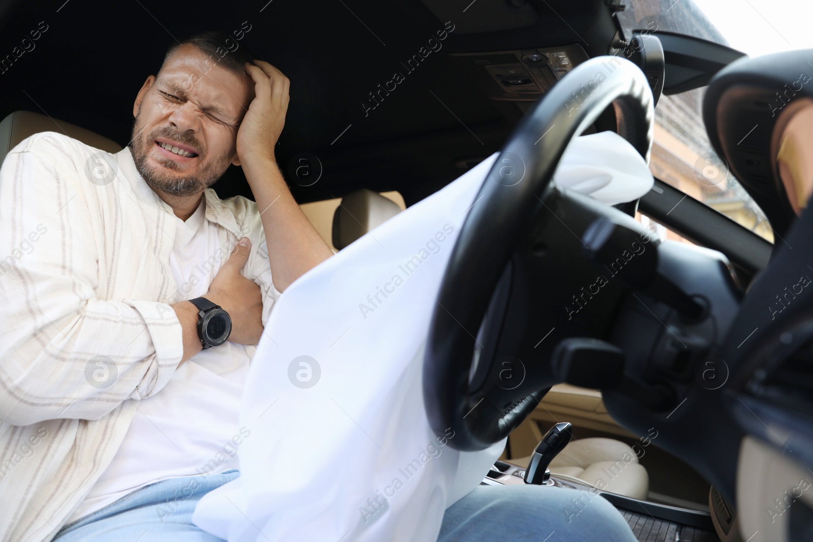 Photo of Injured man near opened airbag in automobile after car accident