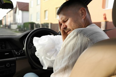 Photo of Injured man near opened airbag in automobile after car accident