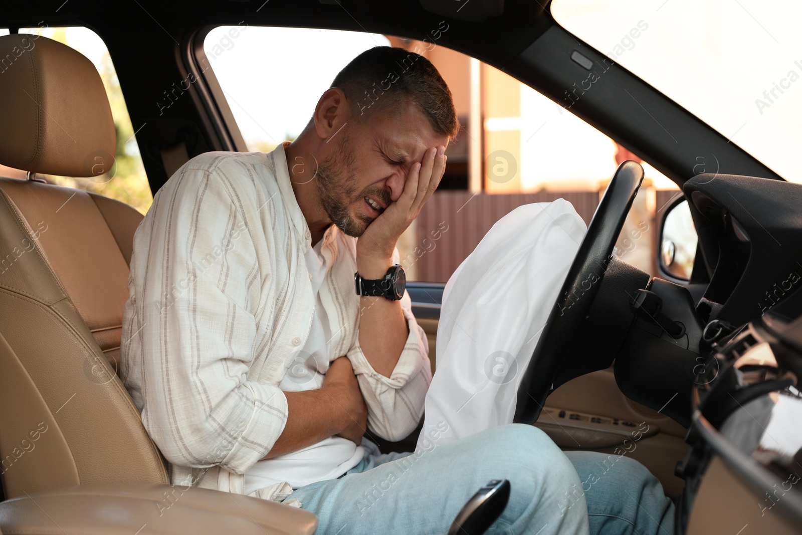 Photo of Injured man near opened airbag in automobile after car accident