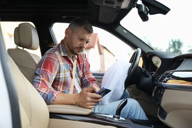 Man using smartphone near opened airbag in automobile after car accident