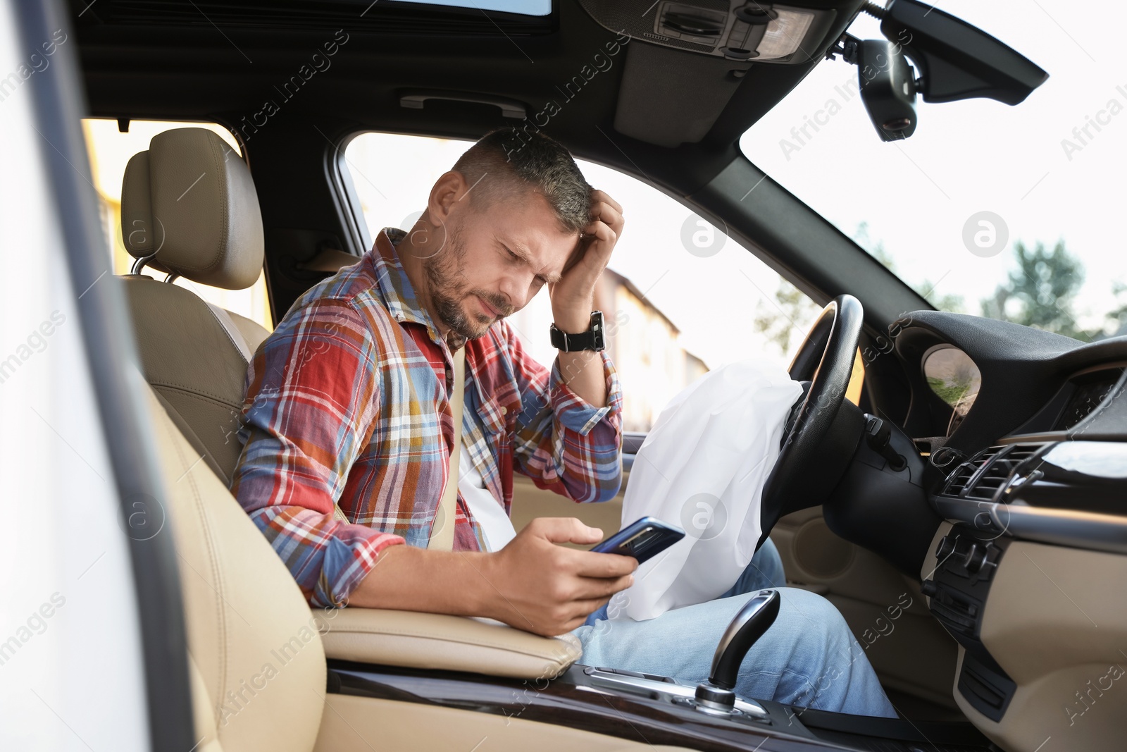 Photo of Injured man using smartphone near opened airbag in automobile after car accident