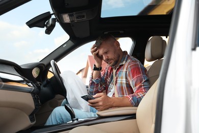 Injured man using smartphone near opened airbag in automobile after car accident