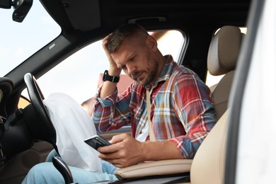 Photo of Injured man using smartphone near opened airbag in automobile after car accident