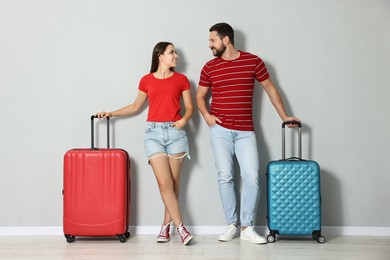 Happy woman and man with suitcases near light gray wall indoors