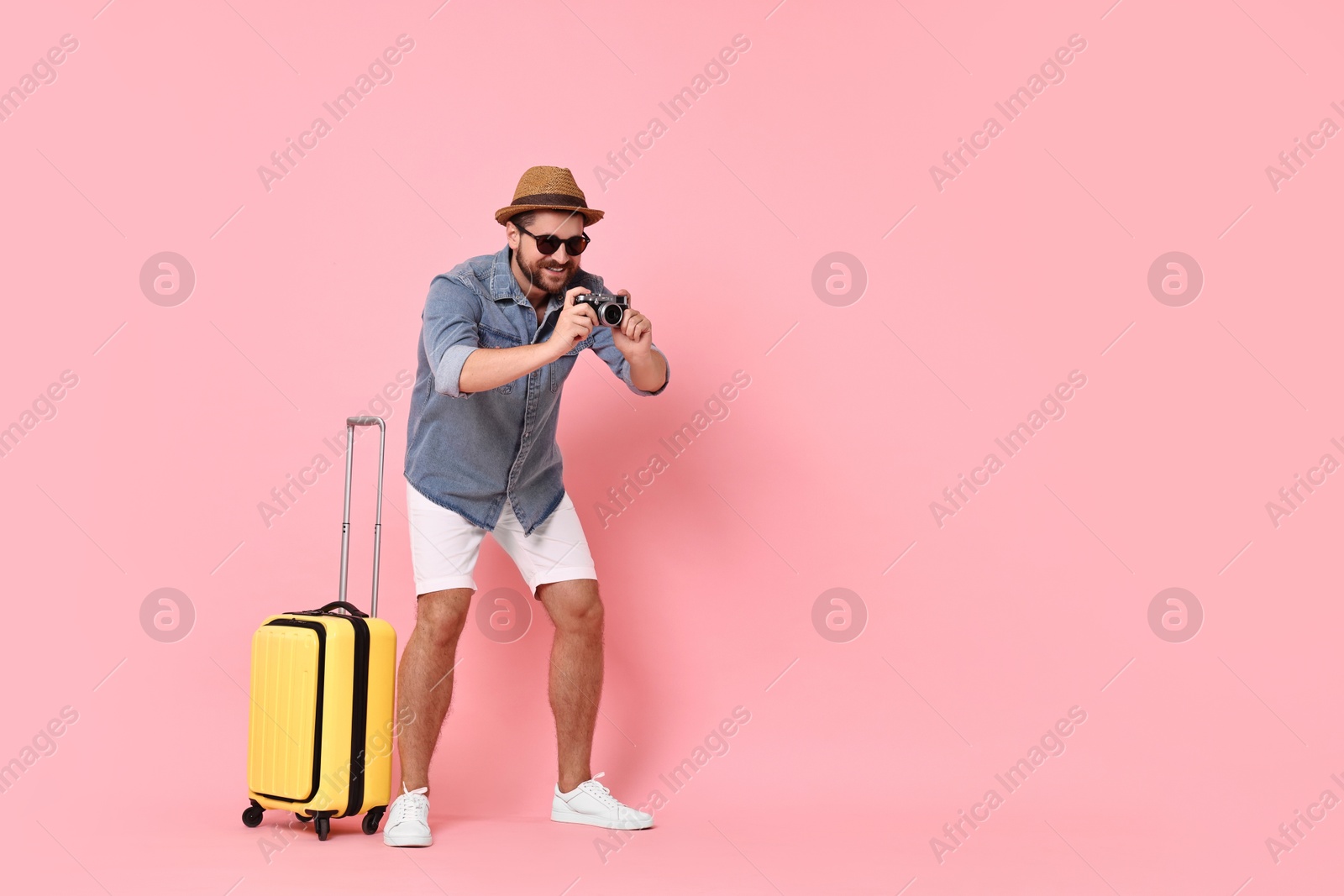 Photo of Happy man with vintage camera and suitcase on pink background, space for text