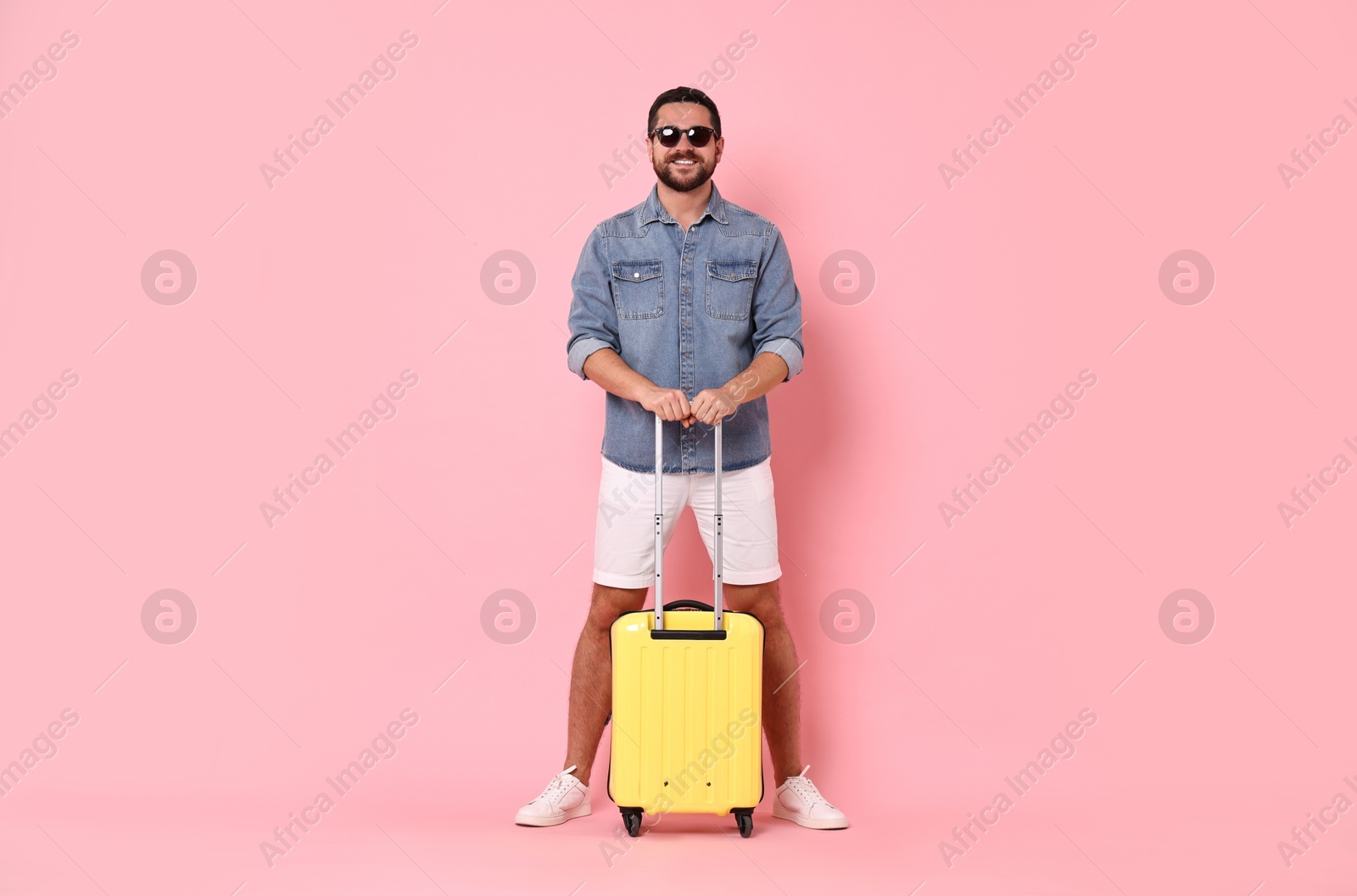 Photo of Happy man in sunglasses with suitcase on pink background