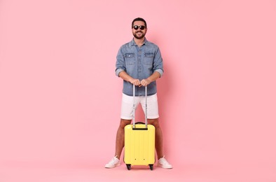 Happy man in sunglasses with suitcase on pink background