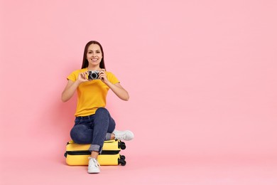 Photo of Happy young woman with vintage camera sitting on suitcase against pink background, space for text