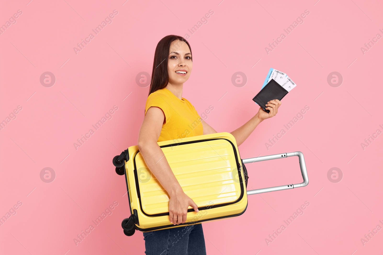 Photo of Happy young woman with suitcase, passport and ticket on pink background