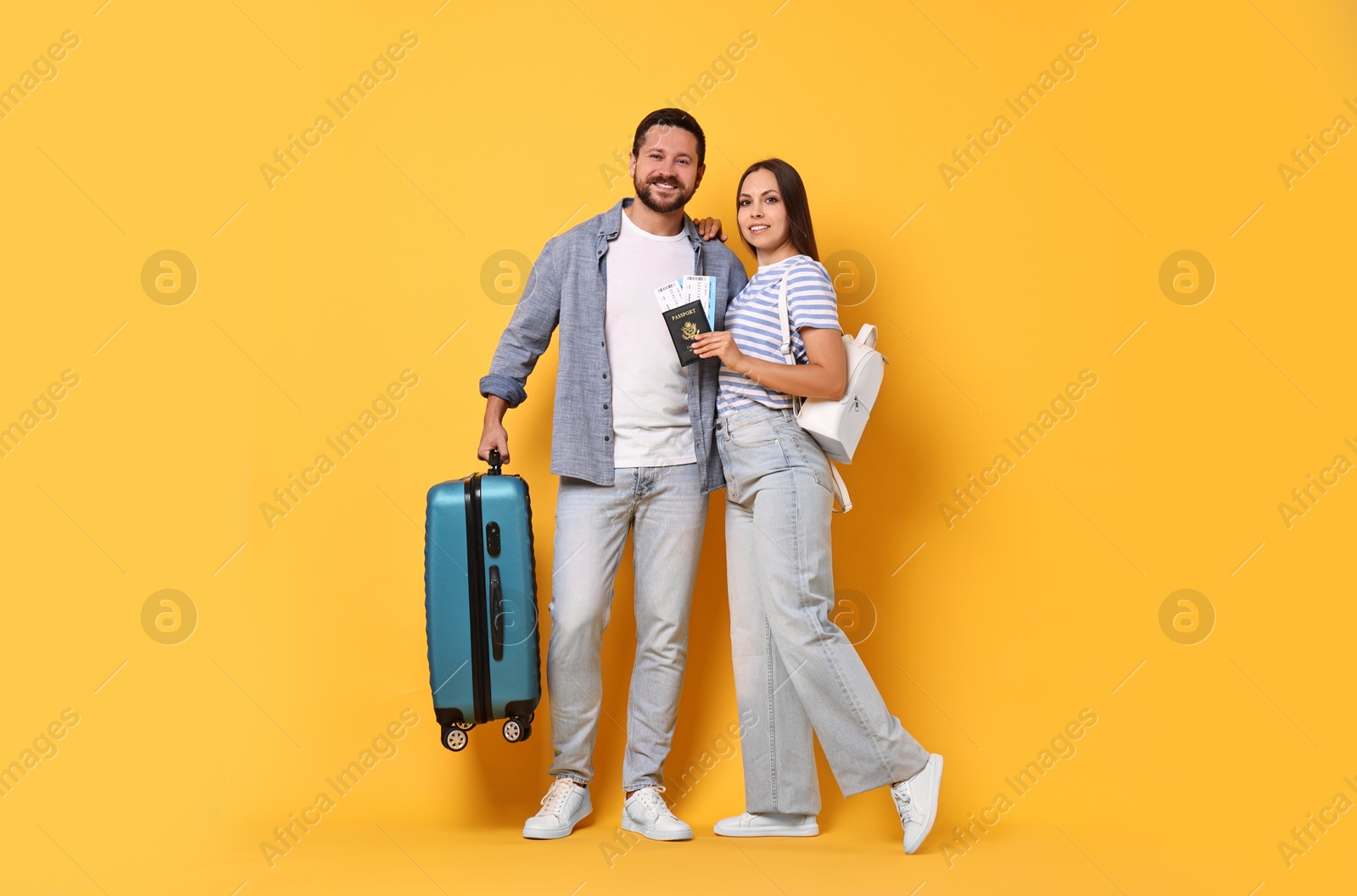 Photo of Happy couple with suitcase, passport and tickets on orange background