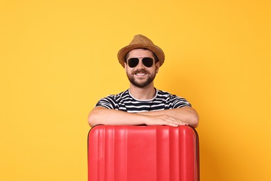 Happy man in sunglasses with suitcase on orange background